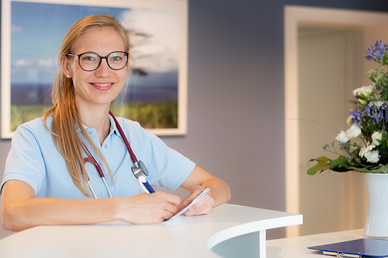 Foto von Dr. med. Anne Pohl Dr. med. Anne Pohl an der Empfangstheke stehend.